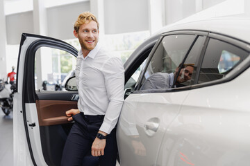 Man smiling satisfied fun customer male buyer client wear white shirt get out car touch door choose auto want buy new automobile in showroom vehicle dealership store motor show indoor Sales concept.