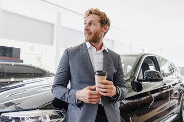 Man minded customer male buyer client in suit choose auto hold cup drink coffee to go look aside want buy new automobile in car showroom vehicle salon dealership store motor show indoor Sales concept