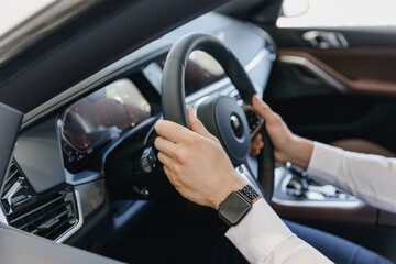 Close up cropped up photo shot hands arms caucasian businessman man wearing white shirt sitting in BMW brand car salon driving hold steering wheel automobile modern vehicle. Car sales driver concept