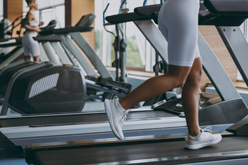 Obraz na płótnie Canvas Cropped up photo shot young skinny strong sporty athletic sportswoman woman wear white sportswear warm up training running on a treadmill in gym indoors. Workout sport motivation lifestyle concept