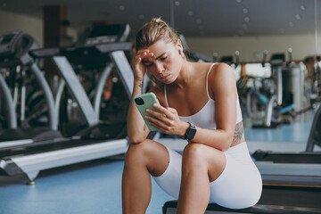 Young pensive puzzled sporty athletic sportswoman woman in white sportswear earphones listen music...