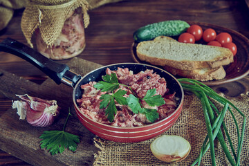 A frying pan with stewed meat seasoned with fresh herbs on a wooden countertop.