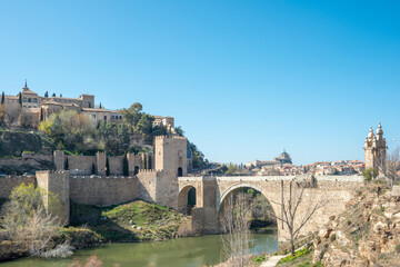 Fototapeta na wymiar Old bridge of San Martín and in the background the monumental city of Toledo. Beneath the arches of the bridge the river Tagus passes placidly.