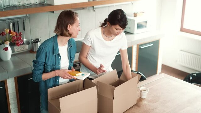 A smiling lgbt couple of girls are unpacking boxes and looking at each other after moving to the new house together