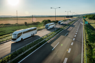 Series of modern White buses traveling on a wide highway in a rural backdrop. Convoy of buses....