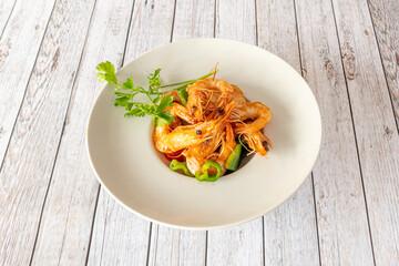 Fried prawns accompanied by sauteed vegetables on a white plate with parsley on a white table.