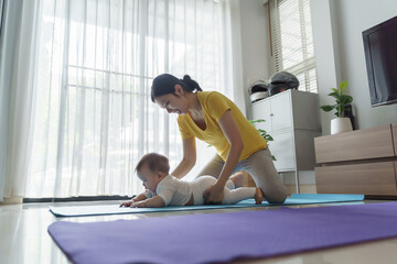 Asian young mother helping her baby learning to crawl on yoga mat