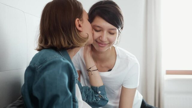 Close-up view of happy lesbian girls expecting a baby and kissing on their belly in the room