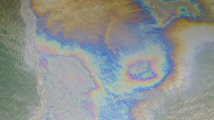 Aerial top down view to the sea surface with the rainbow-colored oil spill pattern