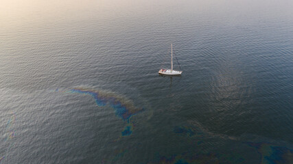 Aerial top down view to the edge of the oil spill leak site with the recreational yacht make way to pass it safely on the Tallinn city area in Baltic Sea, Estonia