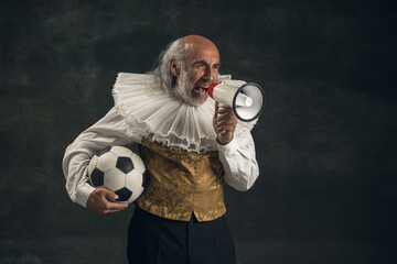 Elderly gray-haired man, actor posing with football ball isolated on dark vintage background. Retro style, comparison of eras concept.