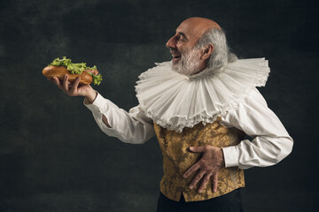 One elderly gray-haired man, medieval hystorical person, actor tasting fast food isolated on dark...