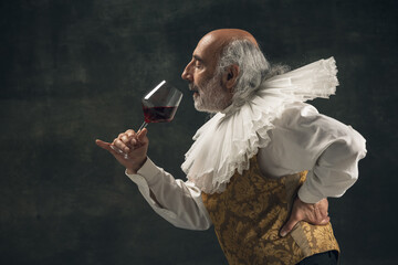 Elderly gray-haired man, medieval hystorical person, actor drinking wine isolated on dark vintage...