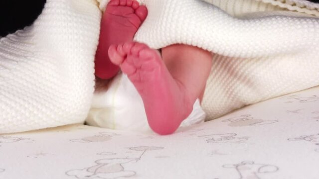 Close up shot of newborn baby in diaper lying on back and jerking her small legs