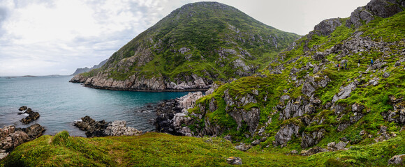 A wide panorama of green hills on the shore of the blue sea on a cloudy day. Scandinavia.