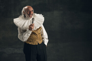 Portrait of elderly gray-haired man, medieval hystorical person, actor singing isolated on dark vintage background. Retro style, comparison of eras concept.