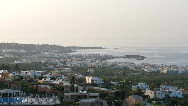 Scenic View Of Hersonissos Town And Coastline In The Island Of Crete In Greece With Calm Aegean Sea On A Sunny Day. aerial static