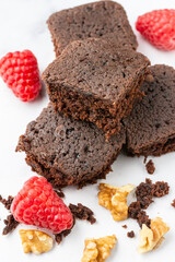 Aerial view of pieces of browni, walnuts and raspberries on white table in vertical