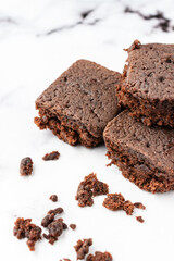 Top view of three pieces of chocolate brownie with crumbs, on white marble table, in vertical, with copy space