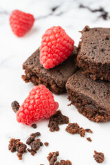 Top view of three pieces of chocolate brownie with crumbs and red raspberries, on white marble table, in vertical