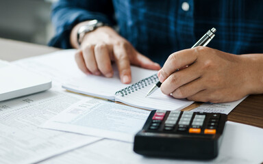 young man holding pen for fill out the document and take note to calculate business data, taxes,...