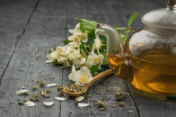 A glass teapot with fresh tea made of jasmine petals on a wooden table.
