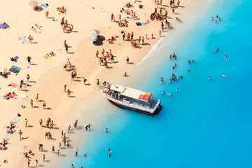 Wall murals Navagio Beach,  Zakynthos, Greece View of Navagio beach, Zakynthos Island, Greece. People relaxing on the beach during their vacation. Blue sea water. A boat drops people off at the seashore. Summer landscape from the air.