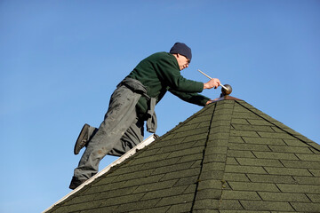Hampshire, England, UK. 2021.  Using a ladder to reach the apex of a garden office to paint the golden ball and surrond on the roof.