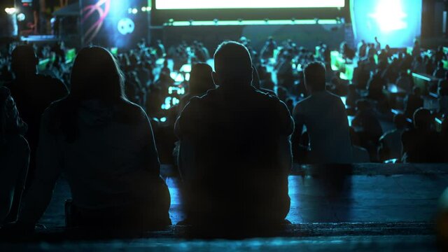 Sitting people watching football in a public place at night