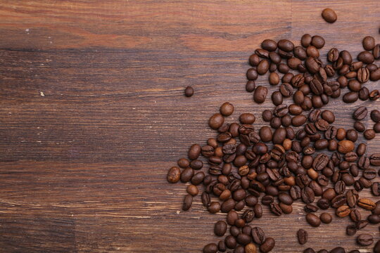 Black coffee grains lie on a brown wooden table, background image