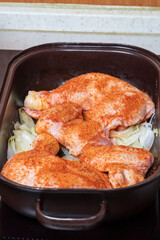 Chicken meat sprinkled with spices is on a baking sheet.