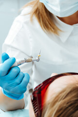 the dentist holds a drilling tool in blue gloves in his hand, over the patient