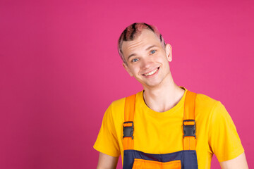 European handsome young man in yellow t shirt and overalls on pink background happy smiling look to camera welcoming