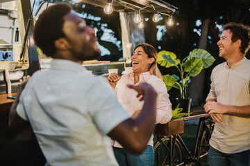 Diverse friends laughing outside food truck in evening