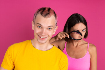 Beautiful modern young couple friends man and woman on pink background holds notebook woman peeks  through magnifier