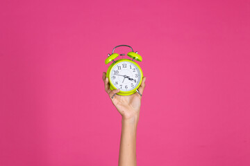 Woman's hand holds green alarm clock on pink background