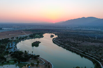 a stunning aerial shot of a sunset over the lake surrounded majestic mountain ranges and lush green trees and grass at Santa Fe Dam Recreation Area in Irwindale, California
