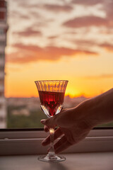 A man's hand with a glass of wine on the background of a bright sunset.