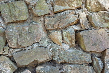 Frontal view of a wall of green and brown granite stones of various shapes and sizes, piled together and held together with cement.