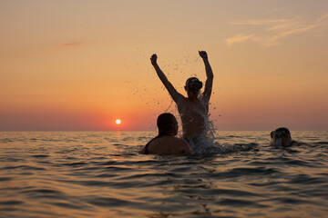 Młodzi przyjaciele kąpią się w morzu o zachodzie słońca. Sepia, backlight, silhouette.