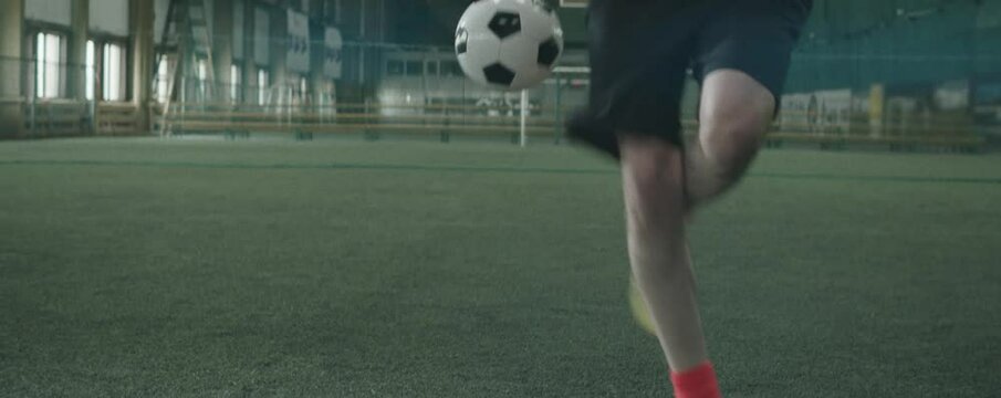 Anamorphic tilt up shot of Caucasian male athlete in sportswear juggling soccer ball on indoor sports field