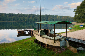 Opuszczona łódź niszczeje na brzegu jeziora. wspomina czasy, kiedy wiatr w żagle i woda pod wiosłami.