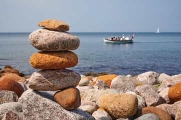 Steinfigur aus Kieselsteinen an einer ruhigen Küste vor einem Ausflugsboot