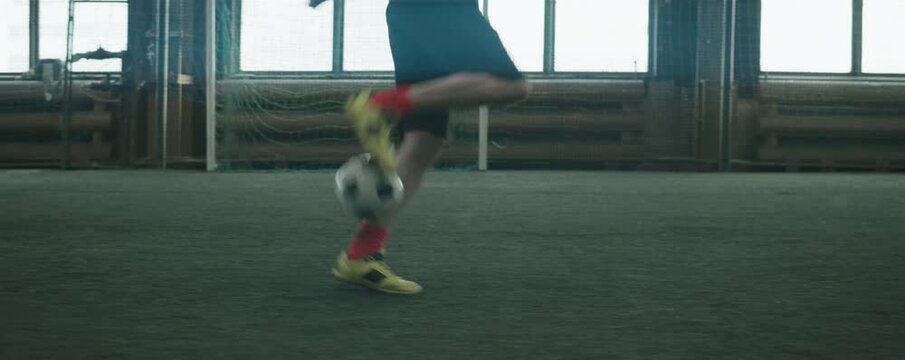 Anamorphic low section shot of legs of professional football athlete in sportswear dribbling ball on indoor field