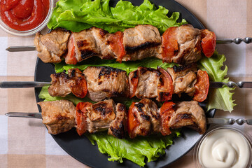 Pork shashlik with salad and lemon wedges on a black plate. Grilled meat on skewers with sauce.