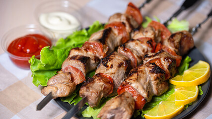 Pork shashlik with salad and lemon wedges on a black plate. Grilled meat on skewers with sauce.