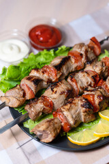 Pork shashlik with salad and lemon wedges on a black plate. Grilled meat on skewers with sauce.