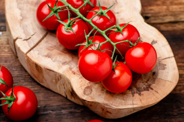 Branch of fresh cherry tomatoes on a brown wooden background.