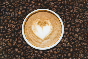 Zenith view of a cup of coffie with a drawn heart  surrounded by coffe beans