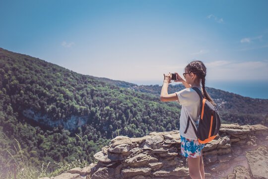 A young girl holds a smartphone to take pictures of a beautiful mountain landscape